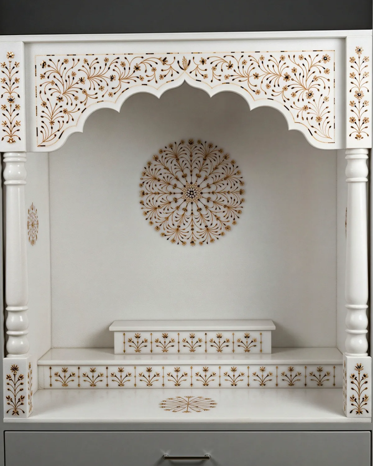 White marble mandir with a scalloped arch inlaid with gold floral vines and a medallion in the sanctum